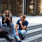 Three young professionals having a friendly chat while sitting on outdoor steps.