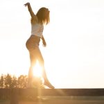 A young woman balancing on a fence during a serene sunrise, exuding freedom and joy.