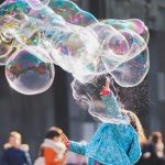 A child delights in chasing and popping giant bubbles in an outdoor setting.