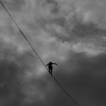 A silhouette of a person balancing on a tightrope against a dramatic, cloudy sky.