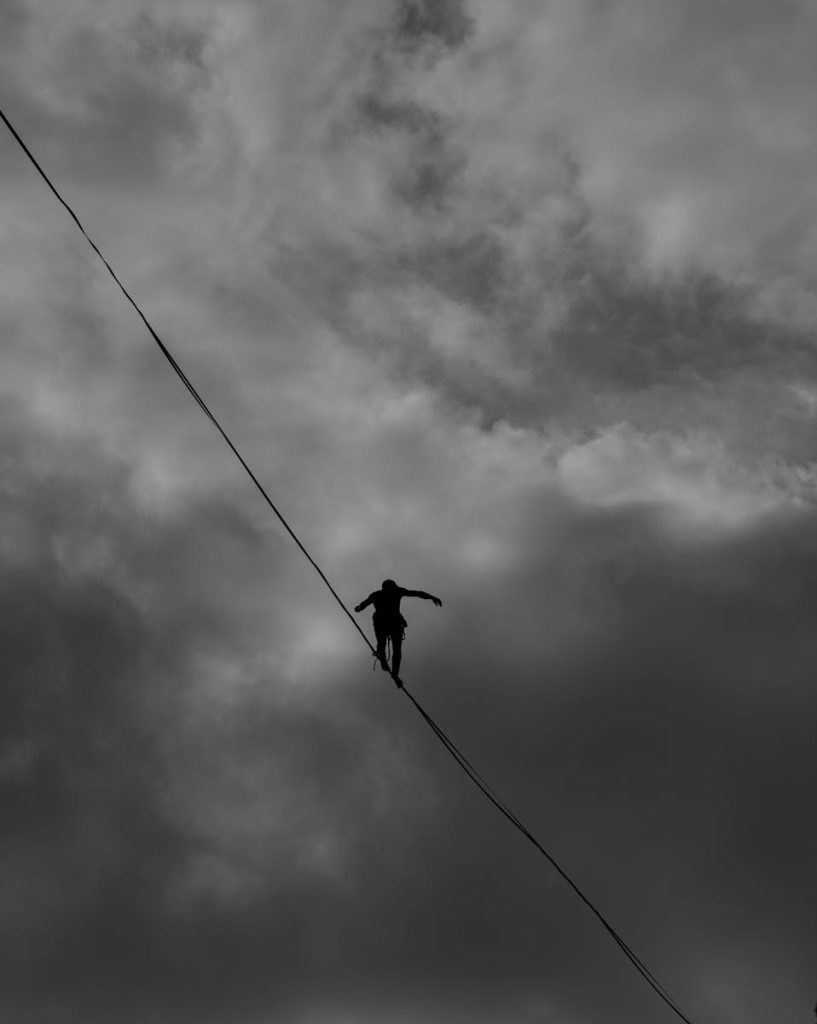 A silhouette of a person balancing on a tightrope against a dramatic, cloudy sky.