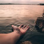 A serene image of a hand touching the water at twilight, creating gentle ripples.