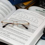 An open book with reading glasses, surrounded by study materials and a laptop, ideal for education themes.