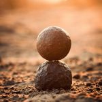 Two stones perfectly balanced on sandy ground at sunset, evoking tranquility and zen.