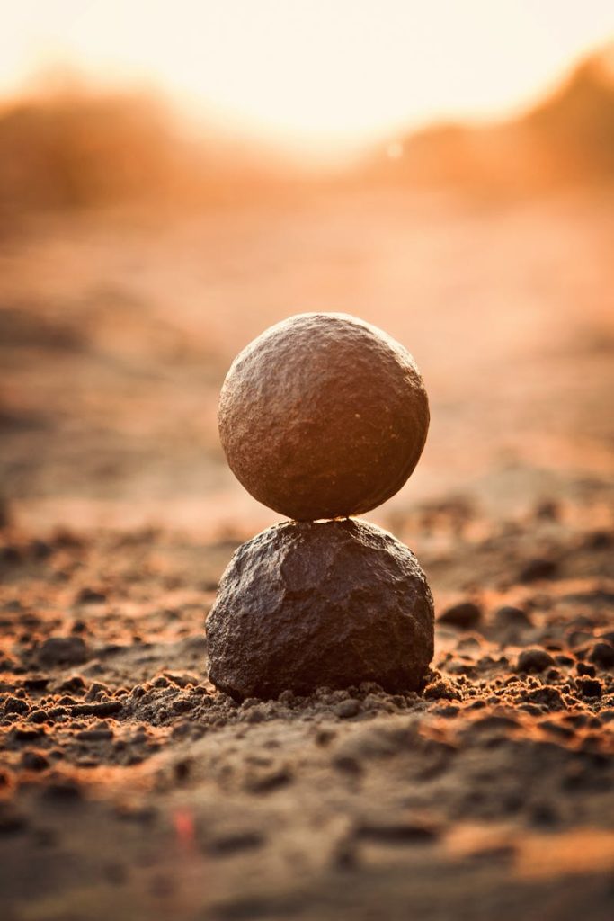 Two stones perfectly balanced on sandy ground at sunset, evoking tranquility and zen.