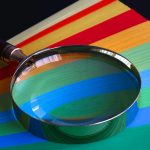 Magnifying glass resting on vibrant rainbow-colored paper close-up.