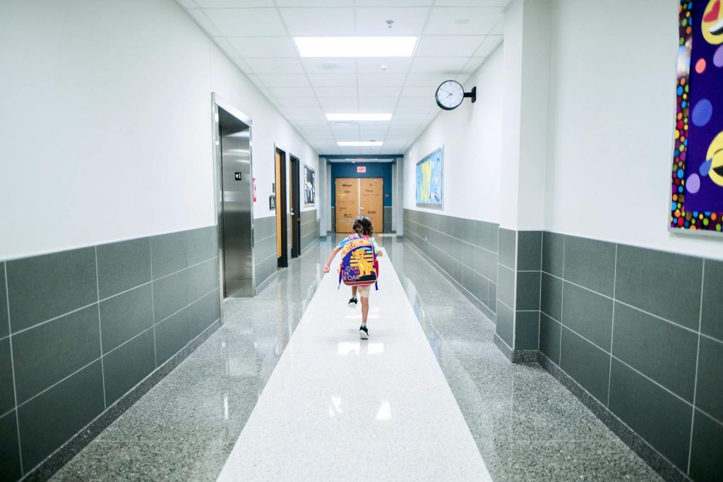 A child runs through a bright school hallway, emphasizing modern architecture and energy.