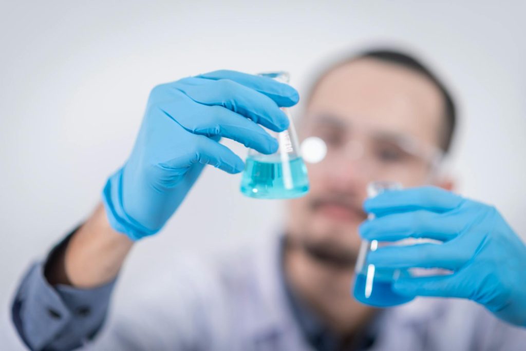 Scientist in a laboratory conducting an experiment, holding blue liquid in flasks with protective gloves.