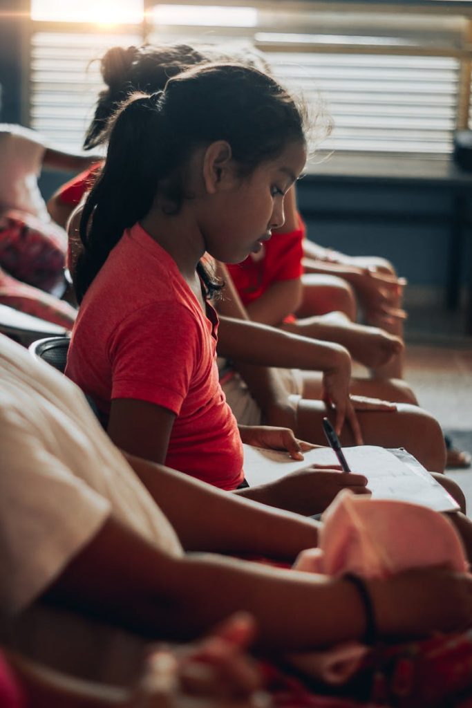 A young girl deeply focused on her studies, sitting indoors during the day.