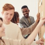 A diverse group of professionals collaborating on a project by using sticky notes on a board indoors.