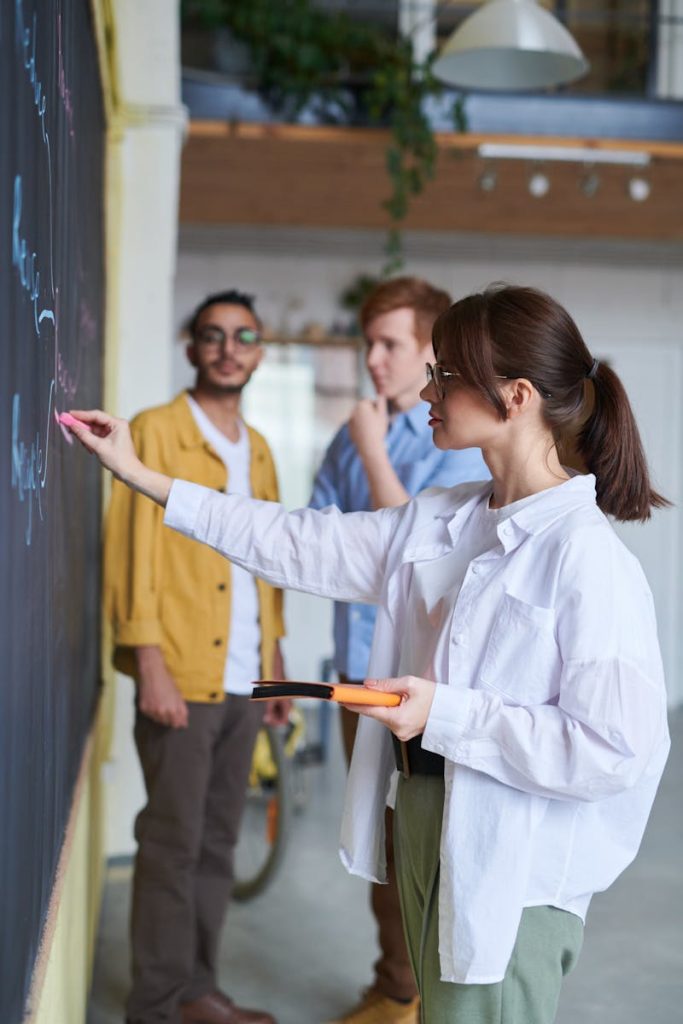 A group of young people discussing ideas at a blackboard in a modern office setting.