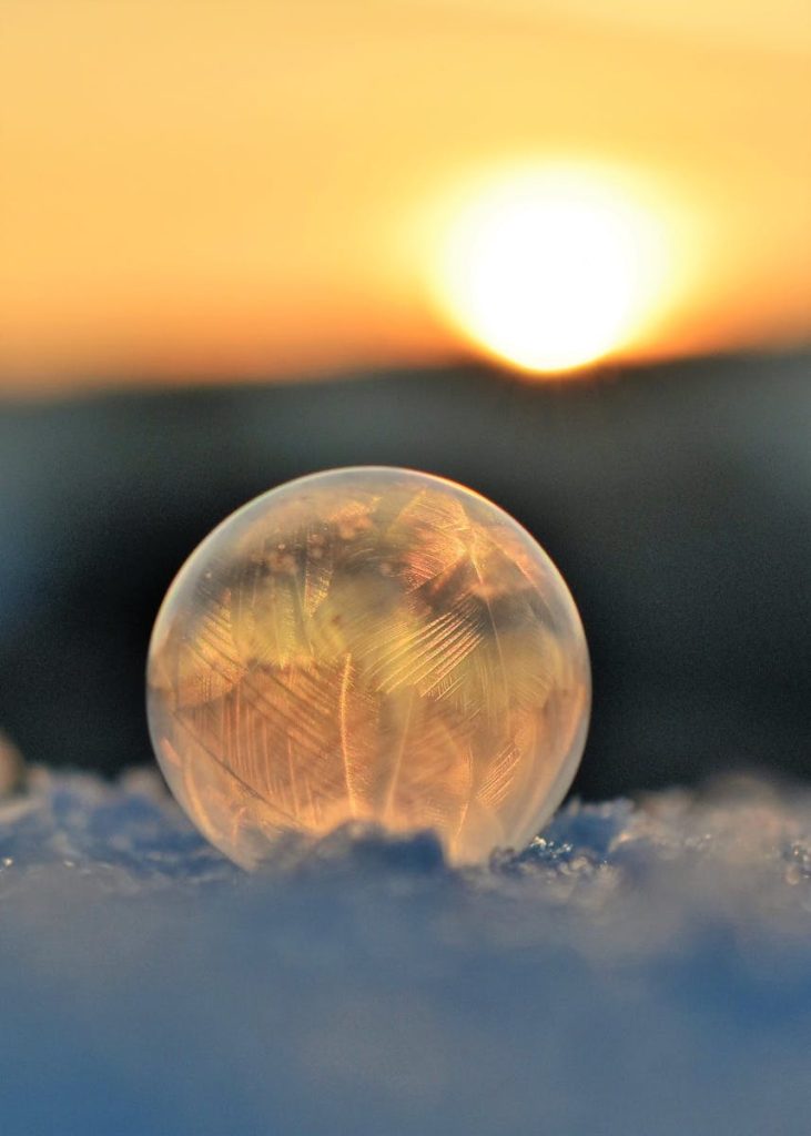 A frozen soap bubble on snow captures crystalline patterns against a sunrise backdrop.