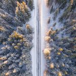 A stunning aerial view of a snow-covered forest with a serene road cutting through. Perfect for winter travel themes.