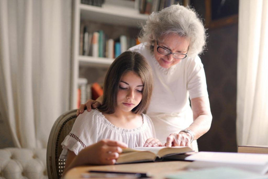 A grandmother and young girl reading a book together in a cozy indoor setting, fostering education and bonding.