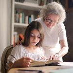 A grandmother and young girl reading a book together in a cozy indoor setting, fostering education and bonding.