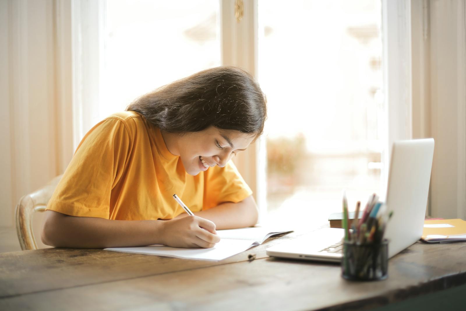 Young woman studying with a laptop and notepad at home, smiling and focused.