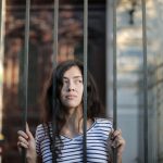 Thoughtful young woman standing behind bars, conveying introspection and solitude.