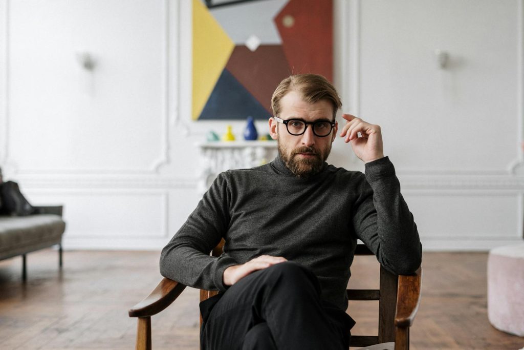 Man with glasses seated in modern interior with abstract art.