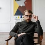 Man with glasses seated in modern interior with abstract art.