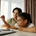 Mother and daughter engaged in online learning at home, using a laptop.