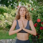 Woman meditating with closed eyes in an outdoor setting, surrounded by nature.