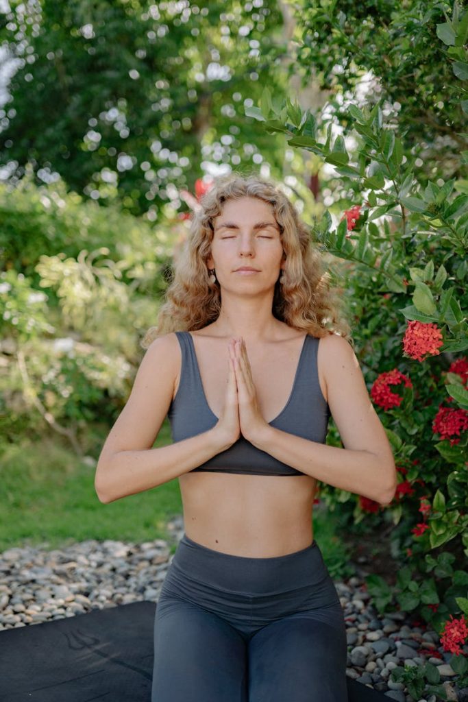 Woman meditating with closed eyes in an outdoor setting, surrounded by nature.