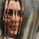 Through glass view of cheerful young female with floral decoration on face looking away