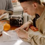 Young student studying with textbooks, calculator, and radio on a sunny day indoors.