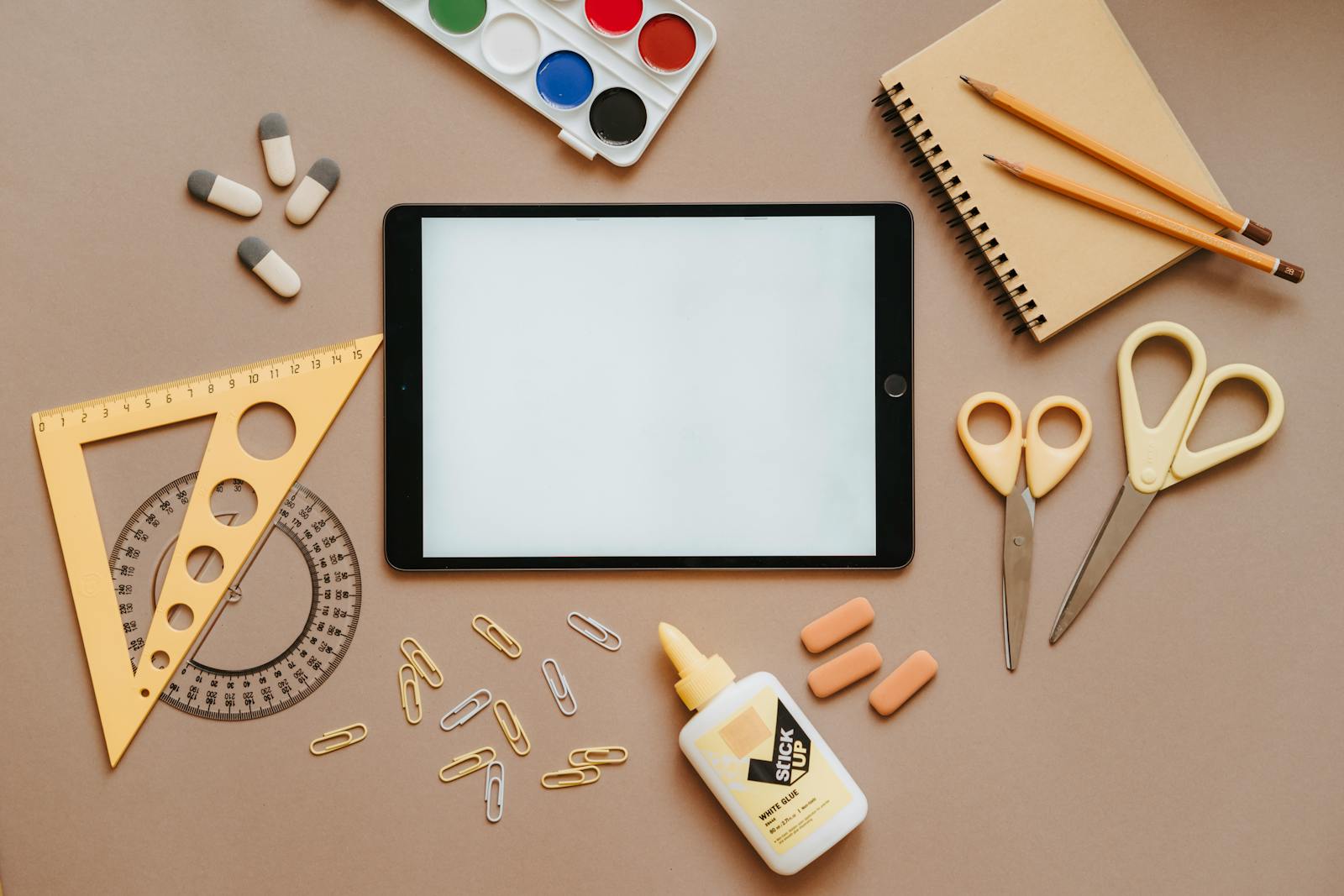 Flat lay of school supplies including tablet, scissors, glue, and stationery. Ideal for education themes.