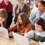 Group of teenagers in a classroom collaboratively working on laptops, fostering team learning.