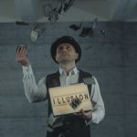 A magician performing a card trick with an 'ILLUSION' sign indoors, creating a mysterious atmosphere.