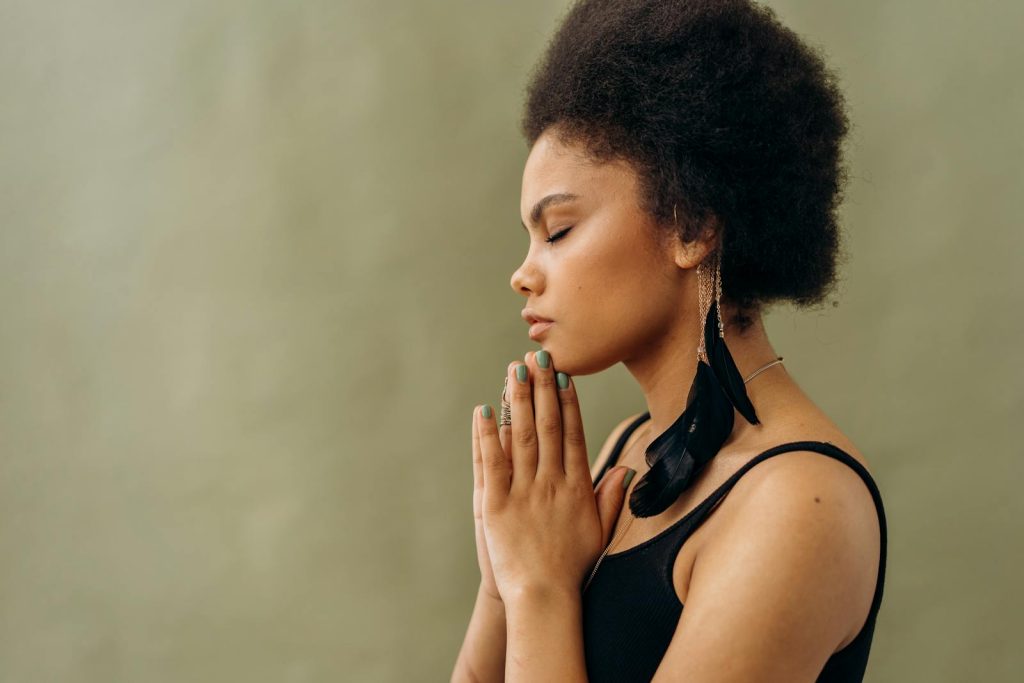 A young woman with afro hair practicing calming meditation indoors.