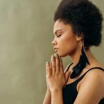 A young woman with afro hair practicing calming meditation indoors.