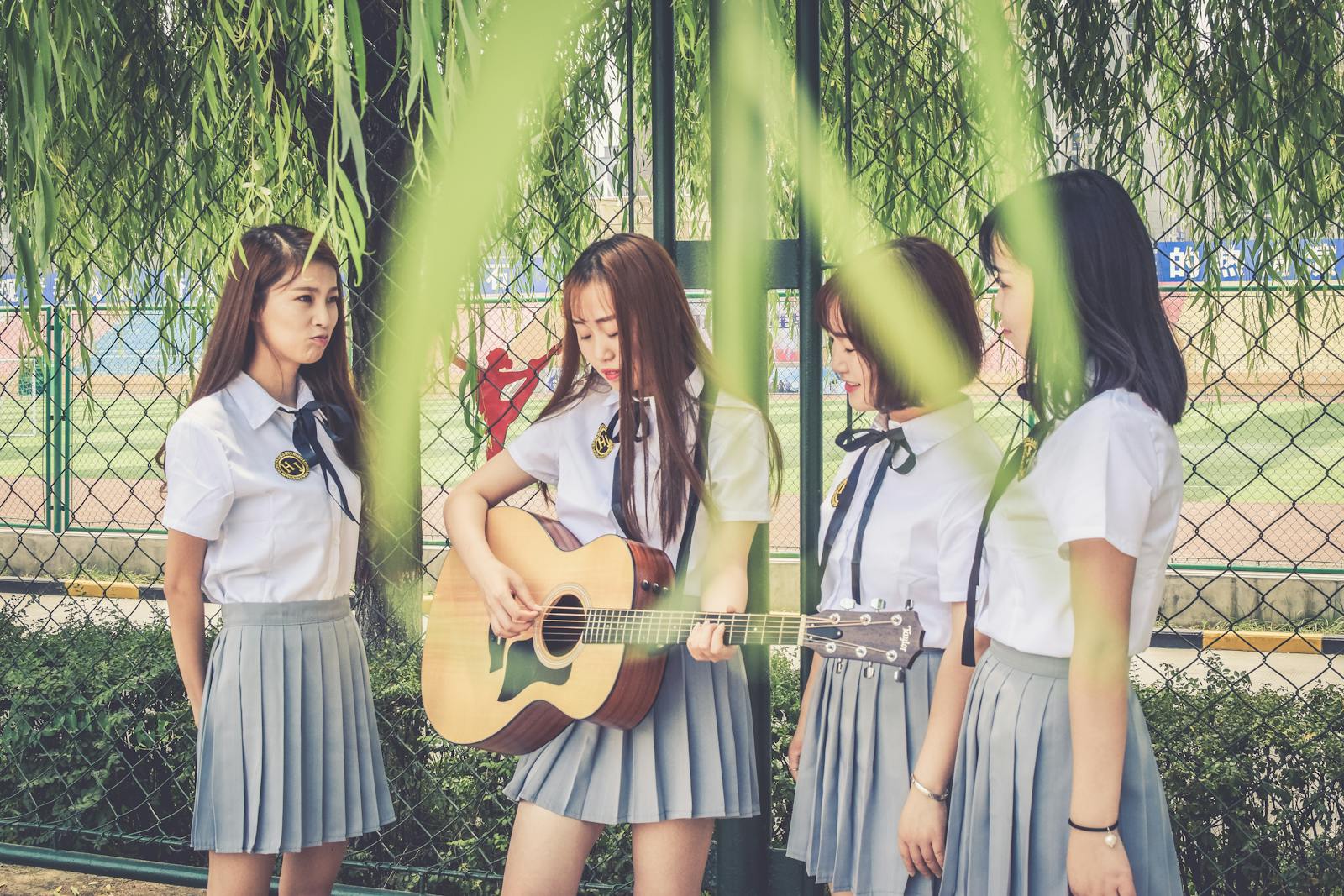 Group of Asian female students in uniform playing guitar outdoors, enjoying leisure and friendship.