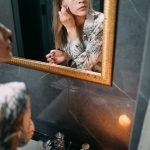 Female using skincare products in a relaxing bathroom with candlelight ambiance.