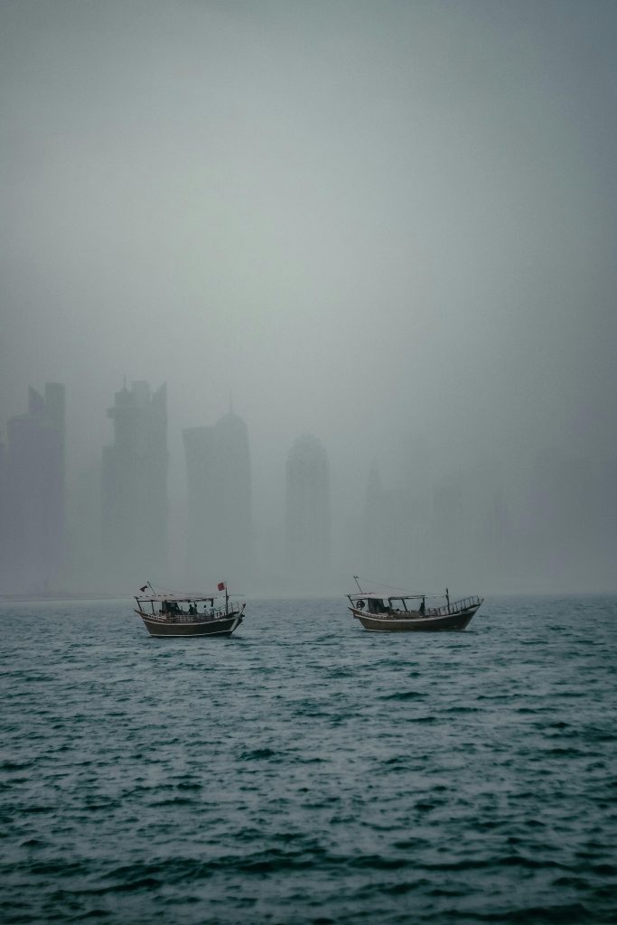 Two boats drift on the sea beneath a foggy skyline, creating a serene morning scene.